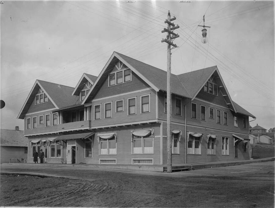 The Potlatch Hotel, which no longer exists. There are two men standing  on side of the hotel. Two things to note in this picture. One, notice on the left side of the building, how far the wooden sidewalk comes out into the street. Second, the electric pole and the many wires leading from it.