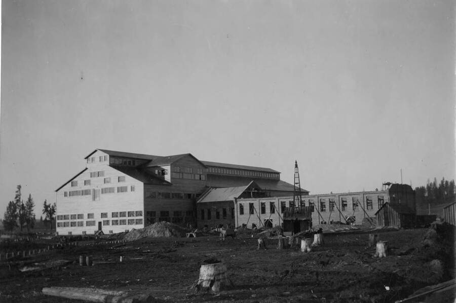 The construction of the mill in Potlatch. The main building is finished, while outbuildings are still being worked on. Several stumps are still in the ground in front of the building.
