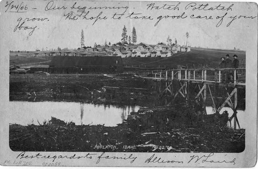 A postcard to Mr. A. W. Morgan in Winona Minnesota. The postcard is showing Potlatch in its early days with three men standing on a wooden bridge looking towards where the mill was being constructed. Written on it, '3/24/06 Our beginning. Watch Potlatch grow. We tope to take good care of your boy. Best regard to family Allison W. Laird.'