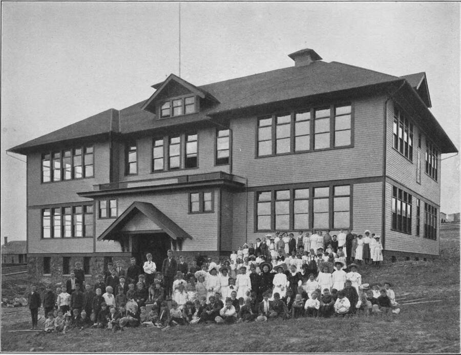 The children of Potlatch schools pose for a photograph in front of the schoolhouse. Scanned from the book 'Potlatch Lumber Company: Manufacturers of Fine Lumber'. The back cover says 'Photographed and published by F. D. Straffin, 336 Riverside Ave. Spokane Wash. Printed by Inland Printing Co. Spokane, Wash.'
