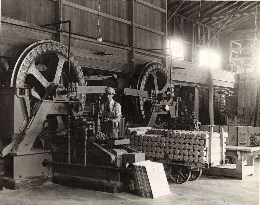 A man stands next to a machine that is making pres-to-logs in the early days.