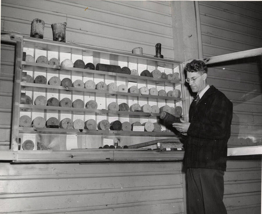 A man holds one of the variety of pres-to-logs, while others are in a display case to his right.