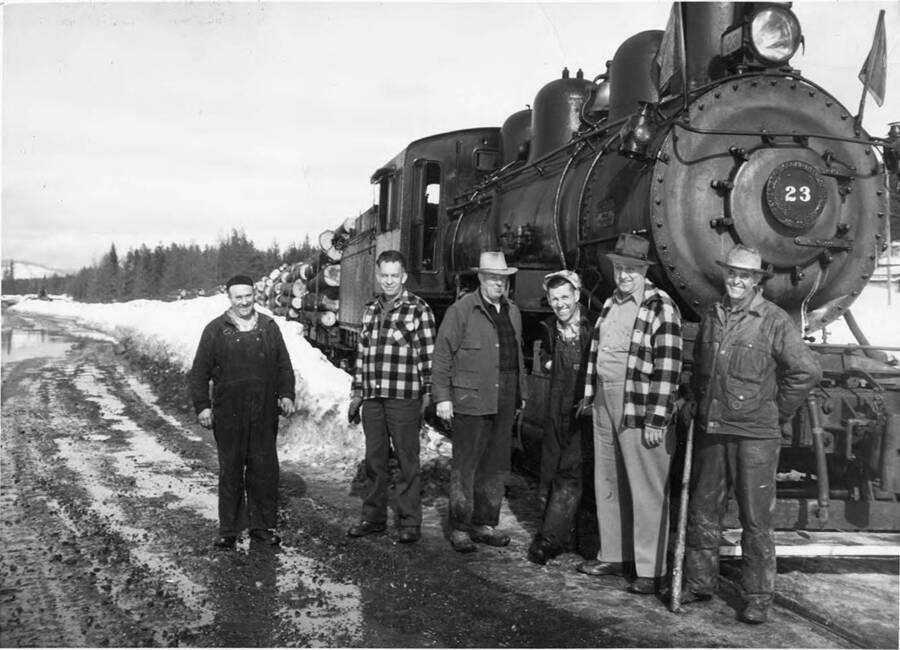 Last run of steam locomotive to Potlatch. Last steam Shay locomotive #107. Train crews were all gone by this time. So John Zagelow took over as engine and byers Sandere as fire man - both Baldwin #23 and Shay #107 were scrapped in 1957. In 1957 steam locomotive #21 pulled 50 year celebrants to Bovill to celebrate 50th year of W.I. & M. entry to Bovill 1907. (description taken from back of photograph) Left to right: Byers Sanderson - Shop Mechanic, John Zagelow - Shop Superintendent, Leslie Mallory - Camp 42 foreman, Kenneth 'Fats' White - Hoister Machinery operator, Axel Anderson - Assistant Woods super under E. Riteheimer, and 'Hap' Hayes - Train crew-conductor.