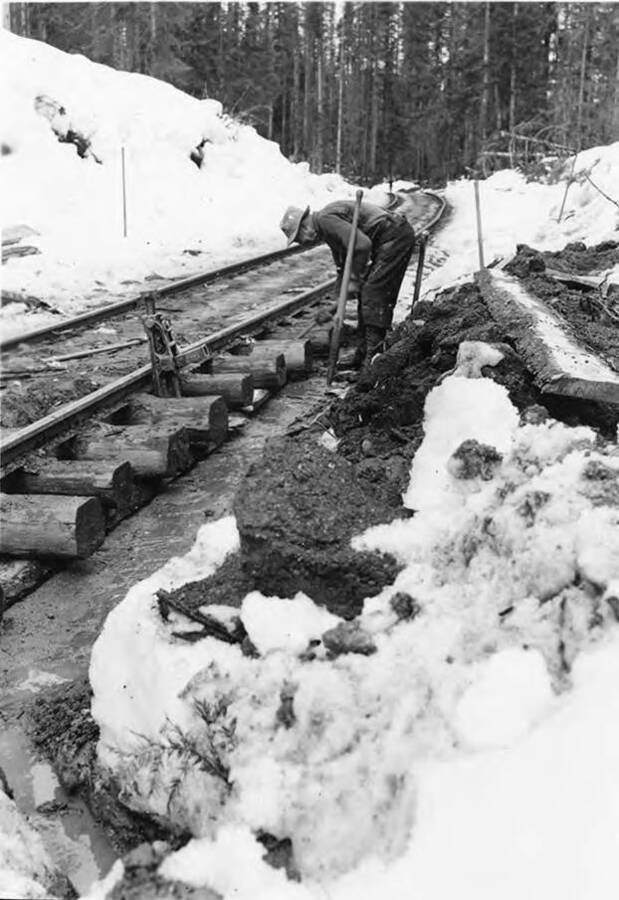 A man works on the railroad ties that hold the railroad track together.