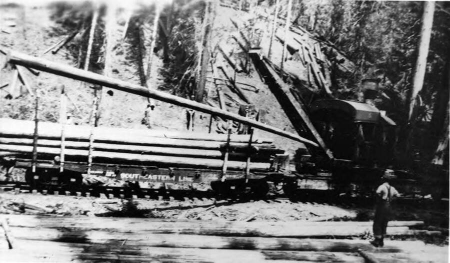 A locomotive crane loads logs onto a flatcar for transport. Description from the envelope 'Elk Basin 1925-1926 loading Gdan Poles with steam loader (No. 2).