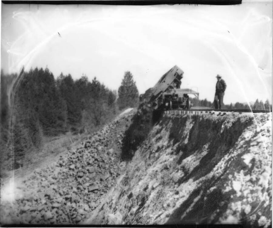 A flatcar on a train dumps dirt and rocks over the side.