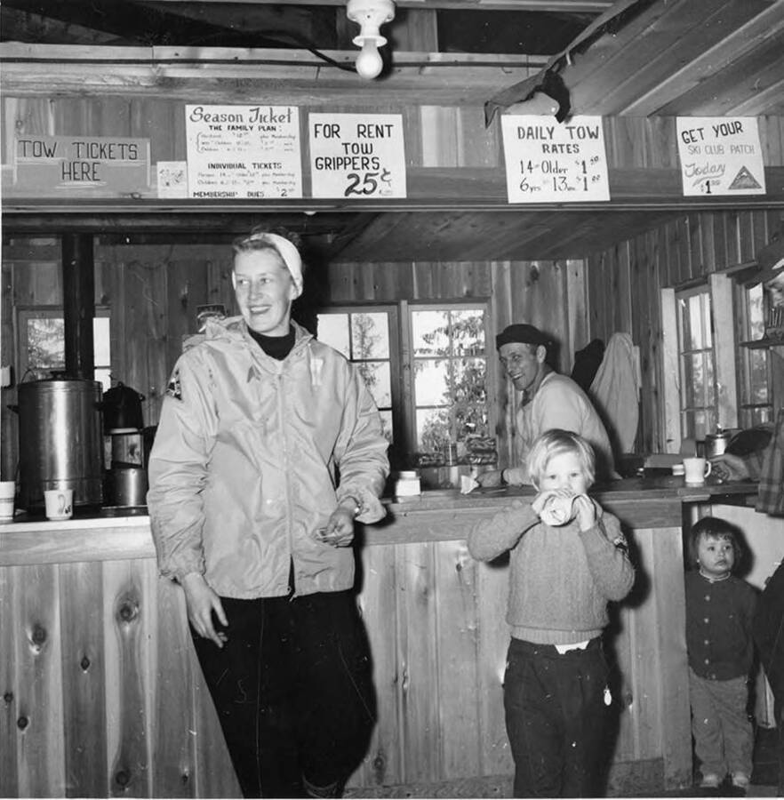 Inside the ski lodge at Bald Mountain Ski area. Two adults, one behind the counter while two children are pictured.