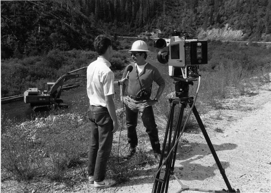 One of the men working on the Orogrande Creek rehabilitation project talks on camera with a member of the media. Behind a piece of equipment can be scene working.