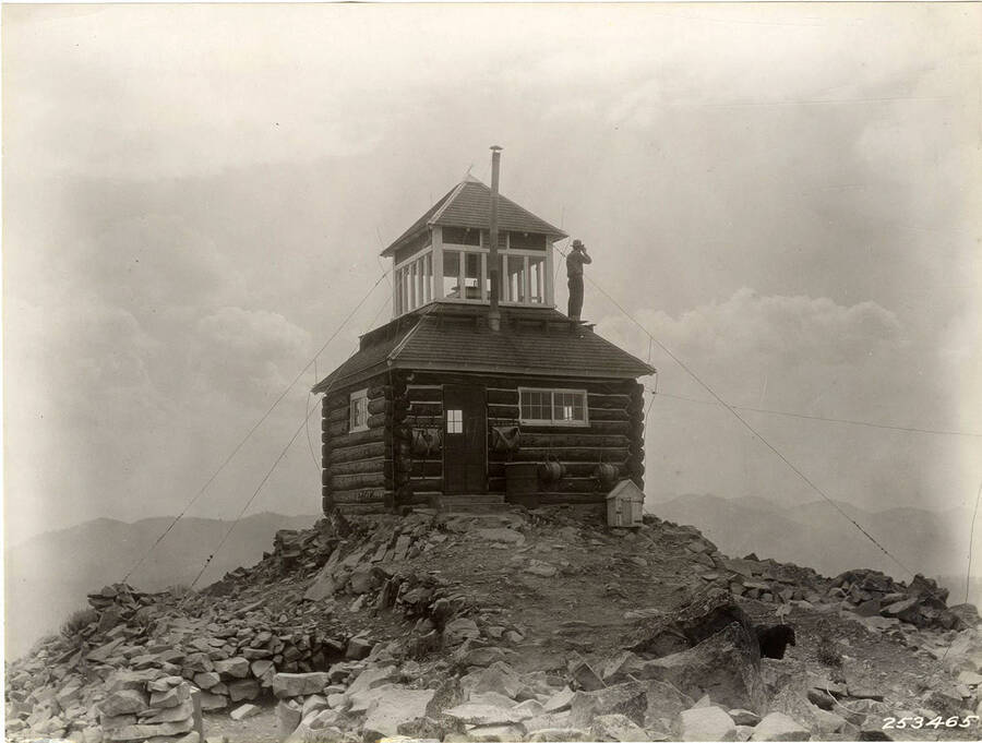 A man stands on part of the roof of the lookout station on Rice Peak.