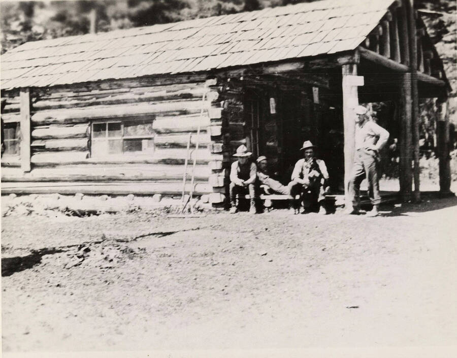 Four men sit on the front porch of a building in Headquarters, Idaho.