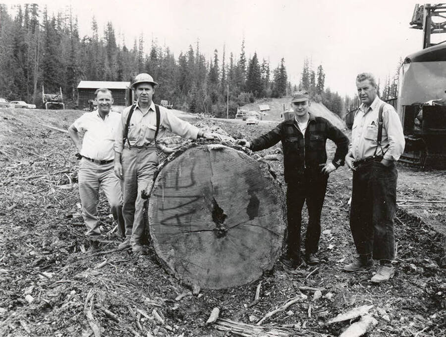 Four men stand in front of the log used for a totem pole at the Iowa State fair.