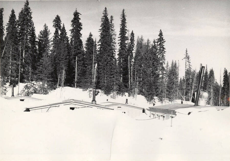 The roofs of camp bunkhouses are very visible due to piled snow.