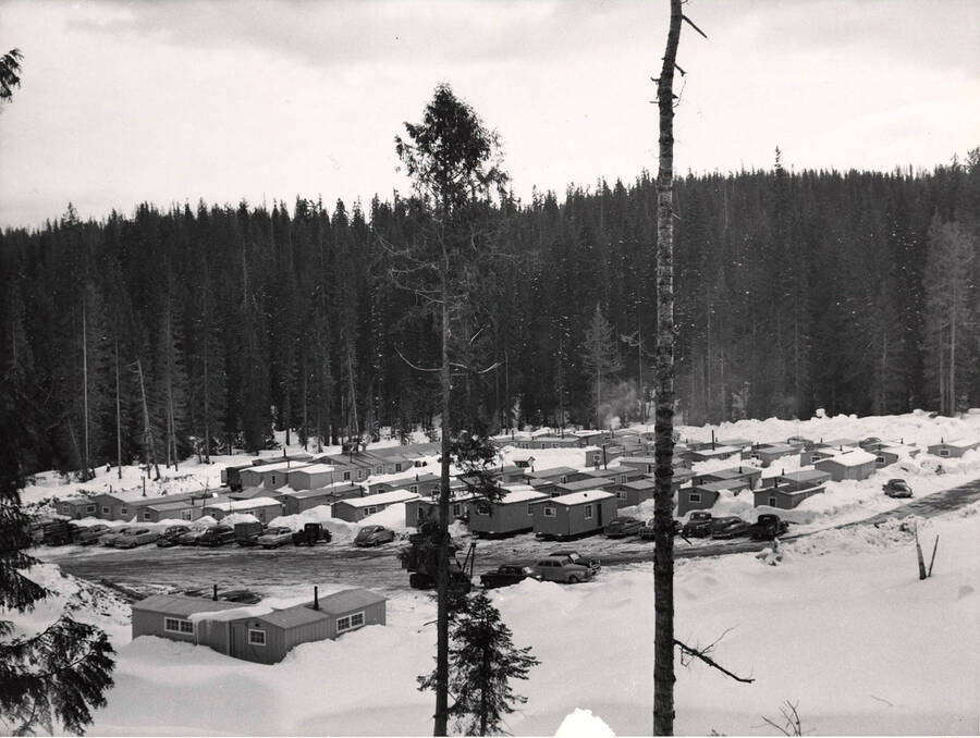 A Potlatch camp in winter. Bunkhouses can bee scene as well as the cars and trucks of the workers.