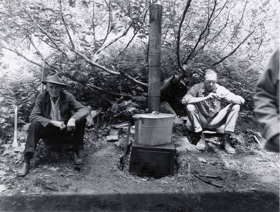 Two men sit near a camp stove at the land board meeting.