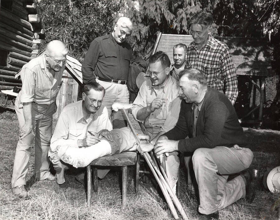 Men gather round at the land board meeting to sign a member's cast on his leg.