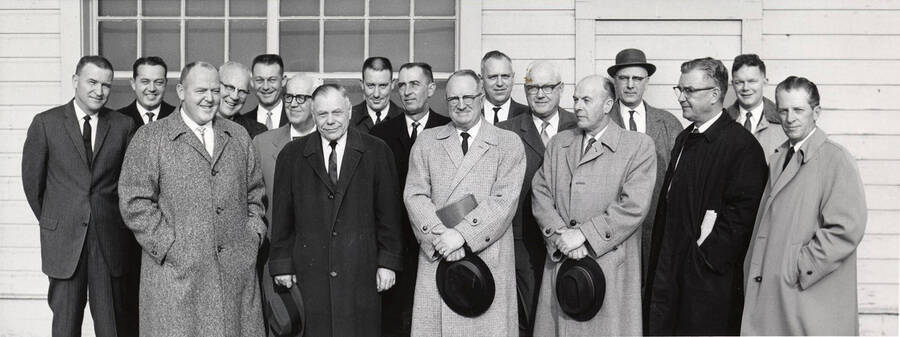 A group of men pose for a picture outside building.