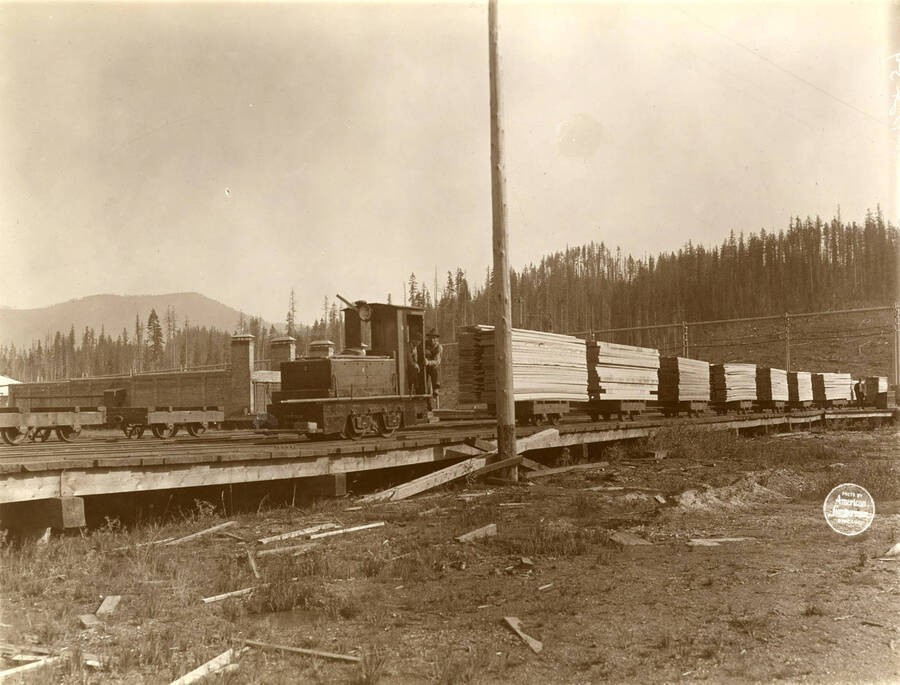 Jeffrey Electric Storage Battery Locomotive and seven tram cars lumber on south track, with dry kilns at back. Description taken from American Lumberman papers found within the folder. Photograph taken between September 28 and October 4.