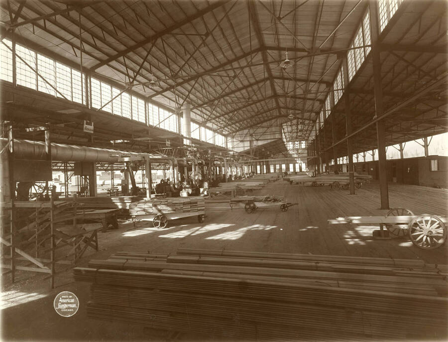 Interior of planing mill from south end, showing from resaw to end of building, and cars on loading dock at right. Description taken from American Lumberman papers found within the folder. Photograph taken between September 28 and October 4.