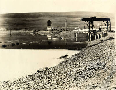 View of the Lewiston Mill from one side of the log pond. In the background is where the logs enter the mill. In the foreground on the right side is a crane-like device to over a railroad track. Written on the photograph (but very faint) is 'CT CO's Plant - 4/30/1928 - No. 265.'