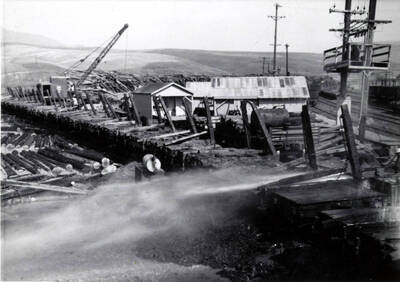 High pressured water is used to clean off log debris from the railcars that brought in logs. In the background, a crane is being used.