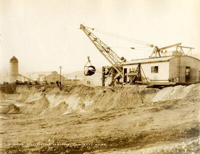 A crane lifts a piece of building material. Two men stand watching. Written on the photograph is 'Winston Brothers Project, 1/8/1927 No. 178.'