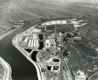 Aerial photograph of the Clearwater Mill. Shown on the left hand side of the photograph and curving around to the top is the Clearwater river. In the center of the photograph is the mill. What use to be the log pond has been filled in and replaced by other structures.