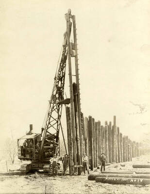 A pile driver attached to a crane is shown while the men using the equipment pose for the picture. Behind them is a row of logs. Written on the photograph is '4/6/1926 No. 14'