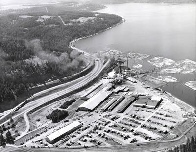 Aerial photograph of the Rutledge Sawmill. In this view, the entire mill can be seen. To the upper right of the mill, are the log ponds and Lake Coeur d'Alene. To the left of the mill is Interstate 90. Stamped on the back of the photograph is: 'Western Ways, Inc. Aerial Photographic Specialists 275 Vera Drive Corvallis Oregon, Phone 35266'