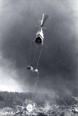 A helicopter uses a drip torch to ignite a controlled burn on a pile of logs.