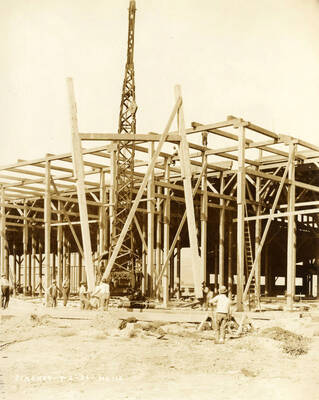 A crane helps lift part of the framing for a building at the Lewiston Mill. Three men help in moving it, while several others watch. Written on the photograph is 'Stacker 9/2/1926 No. 112'