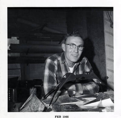 A man uses a stereoscope and aerial photographs to research the forests (description taken from the back)