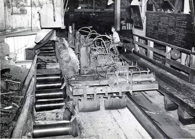 A man works a rough log through a gang saw. The description on the back reads "gang saw in operation."