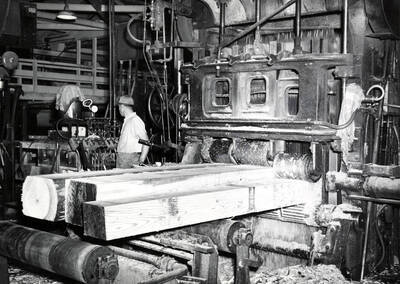 Three pieces of lumber go through a gang saw while a man controls it from the side.
