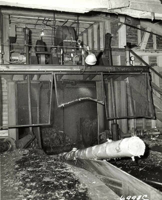 A debarked log is shown either coming out of or going into a piece of machinery. On the right-hand side the machinery, the writing reads "h forests, Potlatch Idaho" and in the lower right hand corner, on the photograph, it is written 6998C.