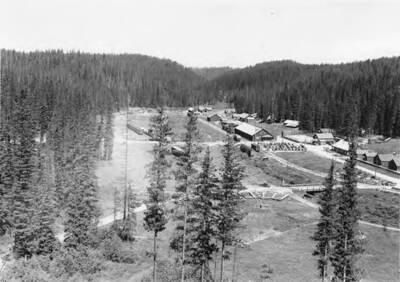A small town in a valley. A bridge over a creek can be seen as well as a lot of parked cars.