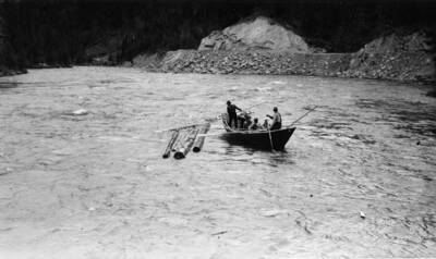 Men use long poles to clear logs that have become stuck in eddies. The description on the back of the photograph reads "men on log drive working in bateaux to clear logs from back eddies."