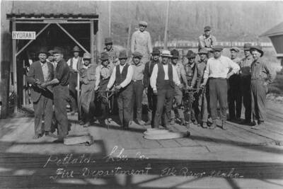 The men of the Elk River, Idaho fire department stand in front of a fire hydrant, posing with hoses.