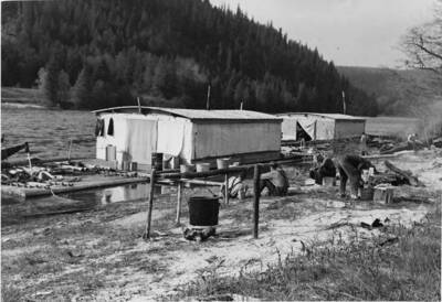 Men sit on shore near the wangian. A pot sits over a fire in the foreground.