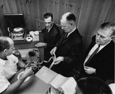Potlatch Forests, INC., management is briefed on operation of the paper tape input-output unit at their newly installed IBM 1710 process control system in the company's Lewiston, Idaho, paper mill. Left to right are: instrumentation engineer Dwain M. Bates, production manager Donald Keller, executive vice president and general manager Edwin C. Rettig and vice president for pulp, paper, and converting Vance V. Vallandigham.