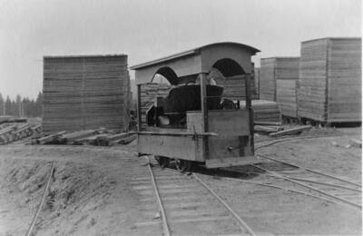 A postcard depicting a vehicle used in lumber yards. Behind it are stacks of board lumber.