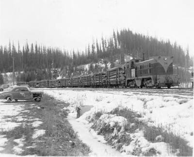 Engine #74 pulls a log train past a 1939-1940 Plymouth Coupe (information taken from back of photograph).