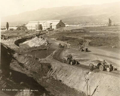 Tractors pulling trailers remove dirt from the south end dyke at the Lewiston Mill.