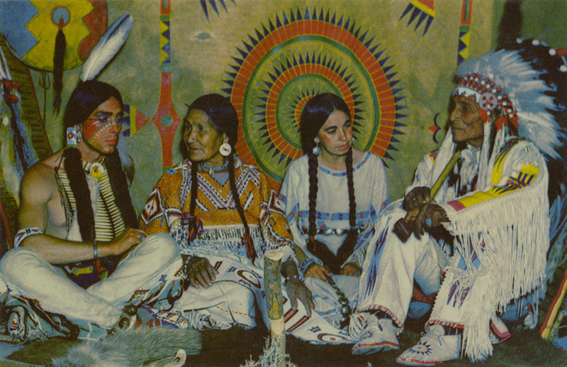 Postcard of a Blackfeet couple meeting with a young entertainer couple in their teepee. | The Laubins-entertainers visiting with the "wades -in-water" Blackfeet Couple, in their teepee.