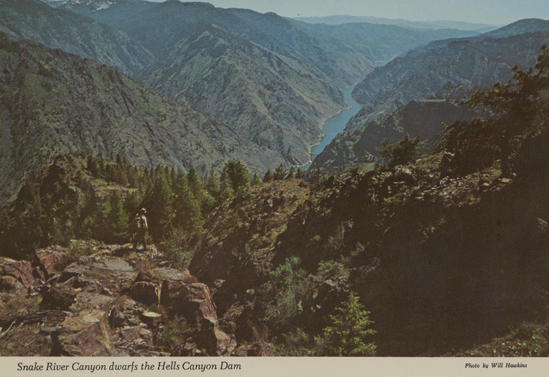 Postcard of a hiker surveying Hells Canyon. | View from Barton Heights, above the heart of Hells Canyon (World's deepest - 7900'), looks south at the backwaters of this Idaho Water Power structure. The river forms a natural boundary between Idaho (far side) and Oregon. Directly below picture point, the river is churned by treacherous rapids and is only navigable by raft with experienced guides. Solitary hiker feasts on the scene from a remote vantage in the rugged Hells Canyon - Seven Devils Scenic Area.