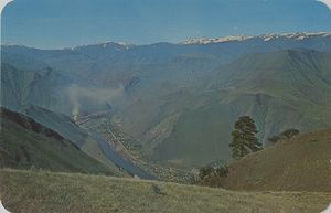 Postcard is of Riggins, Idaho and the Seven Devils mountains in the background. | Spectacular setting of Riggins, the outpost of Idaho's vast Wilderness, located on the Salmon - "River of No Return". Here you see the deepest canyon in the U.S. in which a municipality exists at the bottom: Riggins elevation is 1800. Elevation of the Seven Devils Range is 9410. Just over the Seven Devils Range winds the Snake River in America's deepest Canyon. These two great rivers, so near each other here, appeal to the nation's most daring river-rats.
