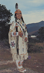 Postcard of Louise Sheryl Edmo. | As Miss Indian America XIX, Louise is well qualified to represent the 800,000 Indians of the United States. Her public experience and knowledge of the problems of her people belie her age. This attractive eighteen-year-old has been a youth delegate to the White House Conference on aging, a delegate to the National Congress of American Indians, Anchorage, Alaska, first runner-up to the title of Miss National Congress of American Indians, besides numerous other recognitions. She plans to attend the University of Idaho to major in political science and pre-law. Louise was photographed in an original designed ceremonial dress of the Bannock tribe, with the Big Horn Mountains in the background. She will reign over the 1973 All American Indian Days and Miss Indian America pageant to be held in Sheridan, Wyoming, July 27, 28, 29.