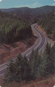 Postcard of Highway 10 in the 4th of July Canyon between Kellogg and Coeur d'Alene, Idaho | Highway 10 in 4th of July Canyon between Kellogg and Coeur d'Alene, Idaho. This northernmost interstate Freeway contrasts vividly with the rugged historic Mullan Trail which traversed this same route a century previous. A treaty was signed on the 4th of July by Indians and Capt. Mullan underneath a white pine tree which still stands near this spot.