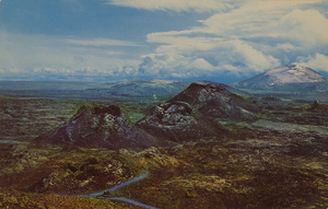 Postcard of spatter cones with a view of surrounding mountains at Craters of the Moon National Monument, Idaho. | Spatter cones in Craters of the Moon National Monument, Idaho. This scenic attraction is located 25 miles southwest of Arco, Idaho, and is easily accessible to tourists on the way to or from Yellowstone Park via U.S. 20.
