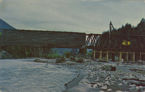 Postcard of the Park Junction Covered Bridge in Pierce County, Washington being demolished.  | Park Junction Covered Bridge World Guide Pierce Co. Wash. One of the few remaining wooden covered bridges owned by the Milwaukee Railroad it is being replaced with a steel bridge. This old twospan bridge is 300 feet long and was built in 1938. Picture taken Sept. 1970 shows one-half bridge demolished and piling driven for temporary track.