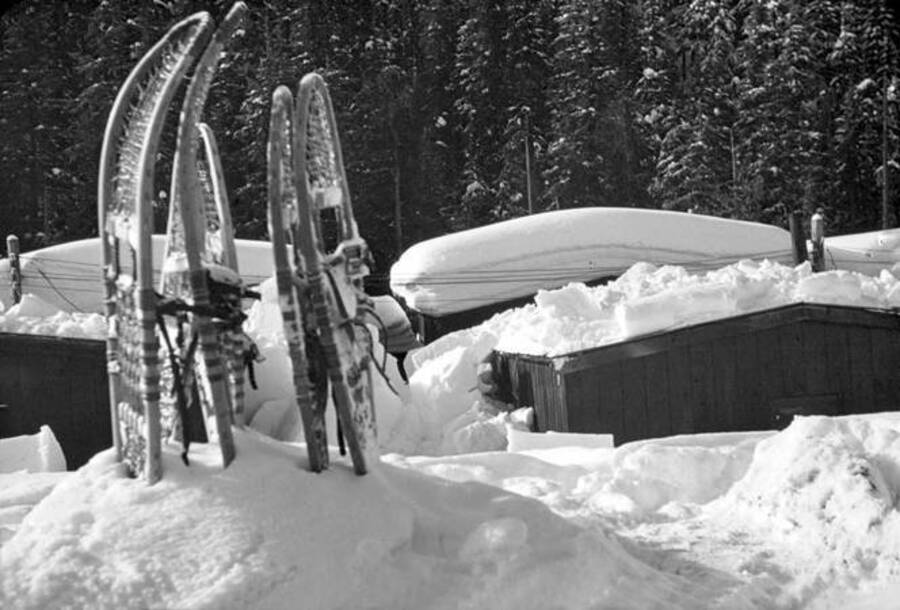 Snowshoes placed in snow. Camp buildings can be seen in the background. Donated by Speed Weidner through Priest Lake Museum.